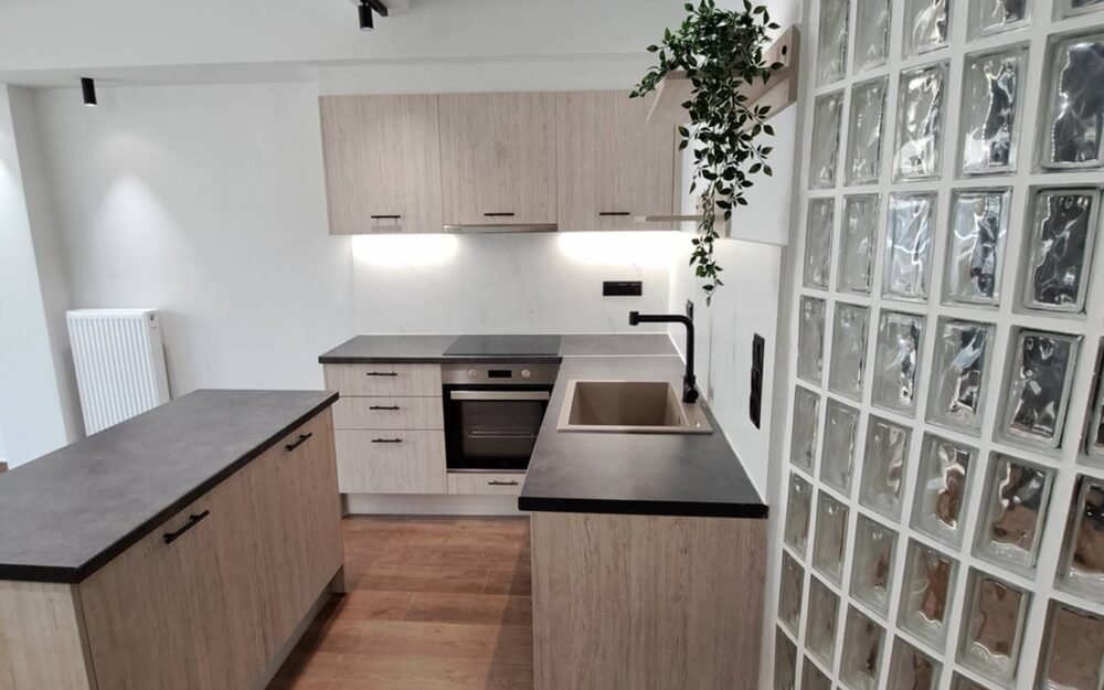 Κουζίνα σε σκούρη αποχρωση, με τοιχο απο υαλότουβλο και νησιδα